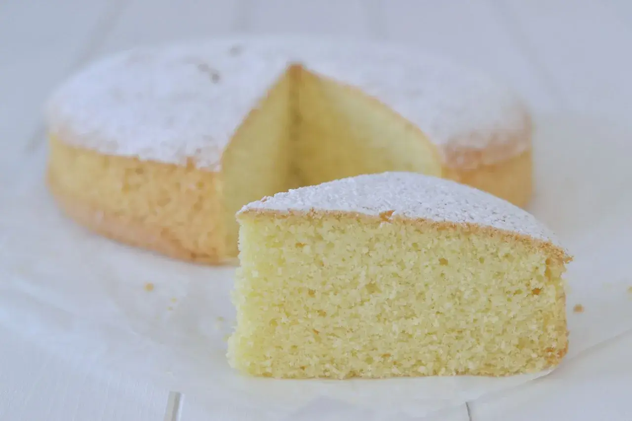 Una soffice torta con farina di riso, spolverata di zucchero a velo, con una fetta tagliata.