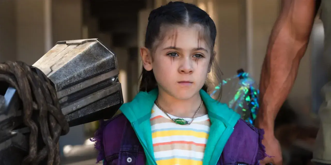 La fille de Thor, avec des marques sur le visage, porte une veste violette et un collier vert. À côté d'elle, le marteau Mjolnir.