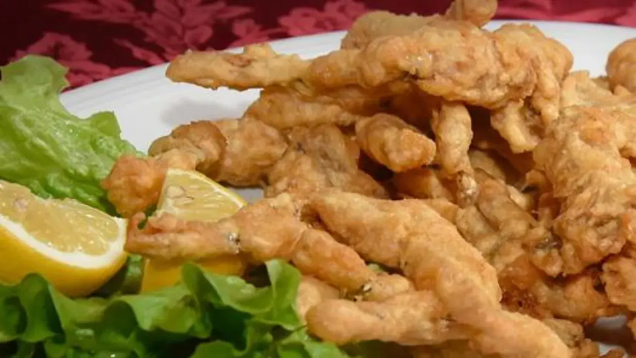 Un piatto di croccanti rane fritte, servite con spicchi di limone e foglie di lattuga fresca.