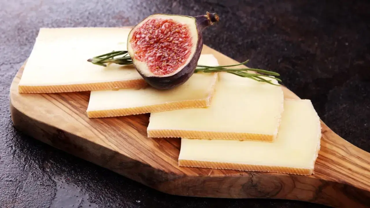 Tranches de fromage à raclette sur planche en bois, garnies d'une figue coupée et de romarin. Parfait pour une recette raclette 6 personnes.