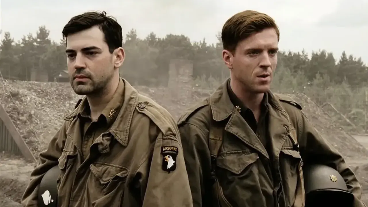 Dwóch żołnierzy w mundurach, symbolizujących bandę braci, stoi na tle zniszczeń. Jeden z nich ma naszywkę "AIRBORNE".