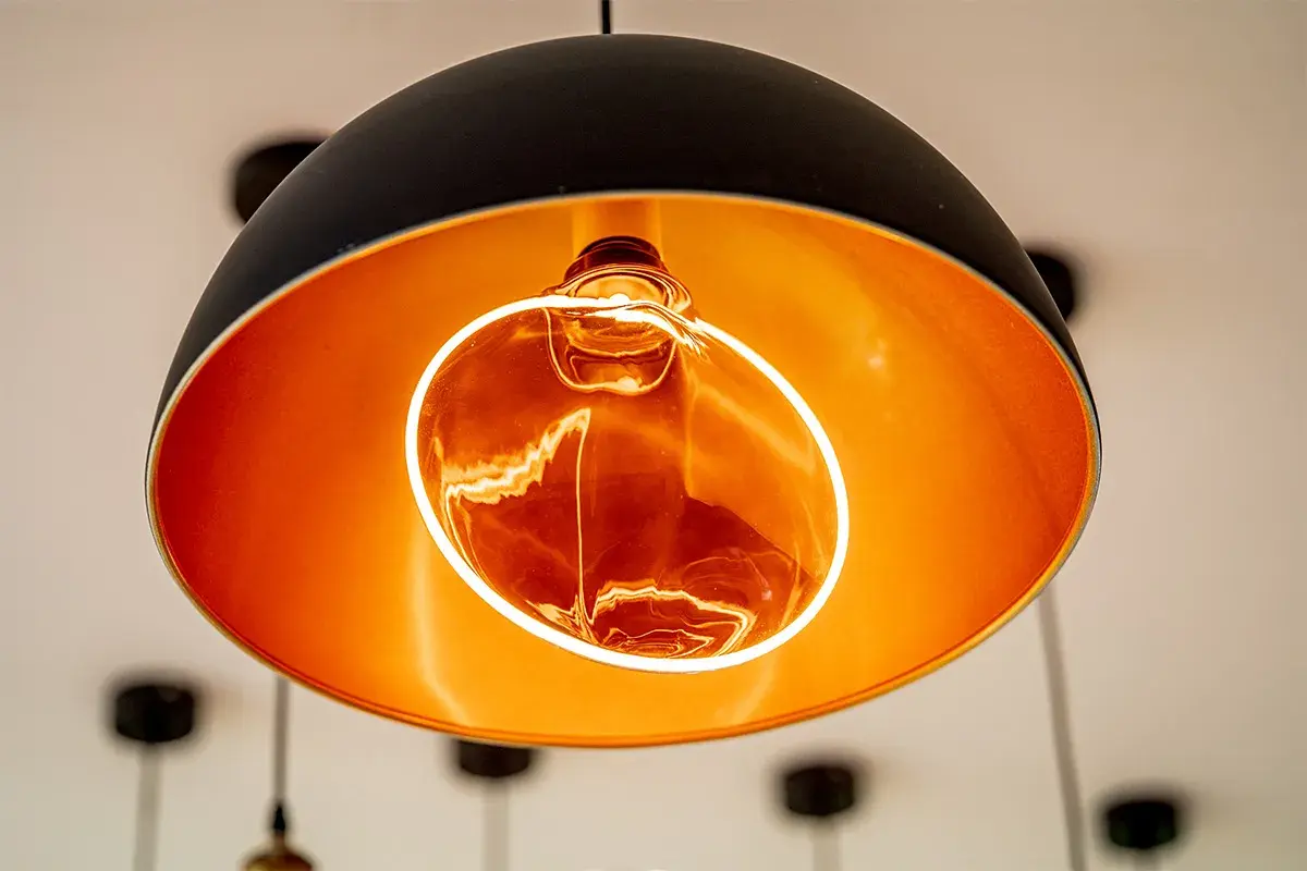 Lámpara colgante moderna con interior dorado y una bombilla decorativa Edison encendida, creando un ambiente cálido.