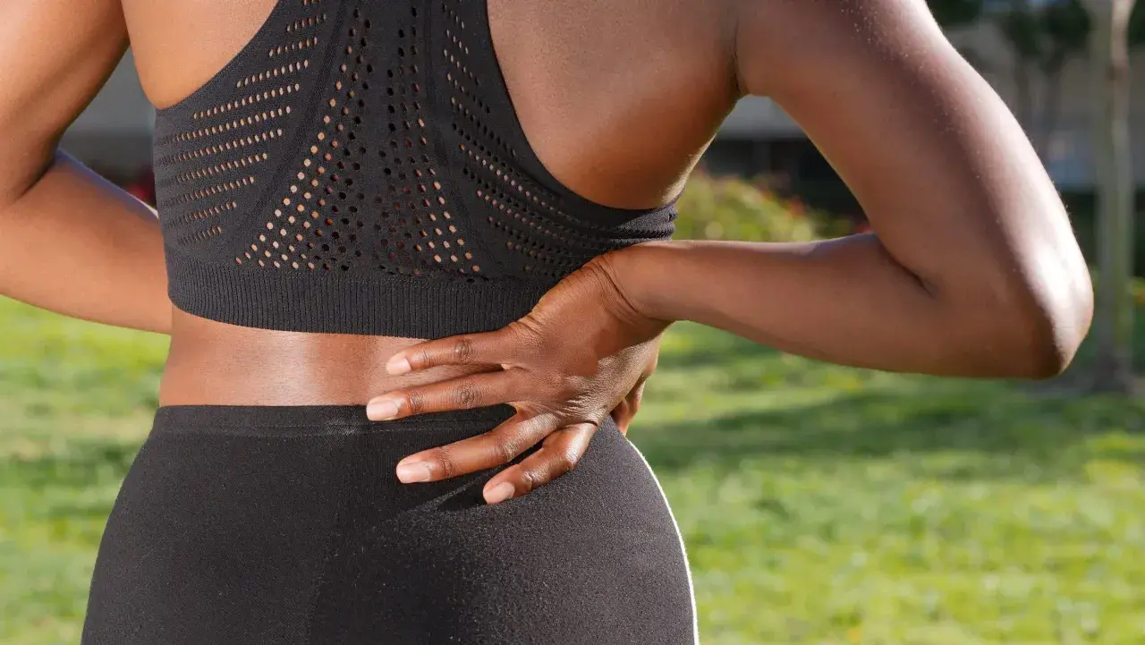 Une femme en tenue de sport ressent une douleur barre dans le dos, sa main posée sur la zone sensible.