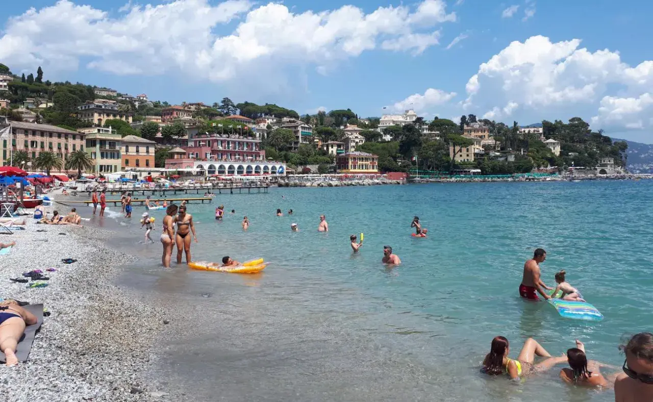 Journée ensoleillée à la plage Santa Margherita Ligure, baigneurs profitant de la mer turquoise et des bâtiments colorés en arrière-plan.