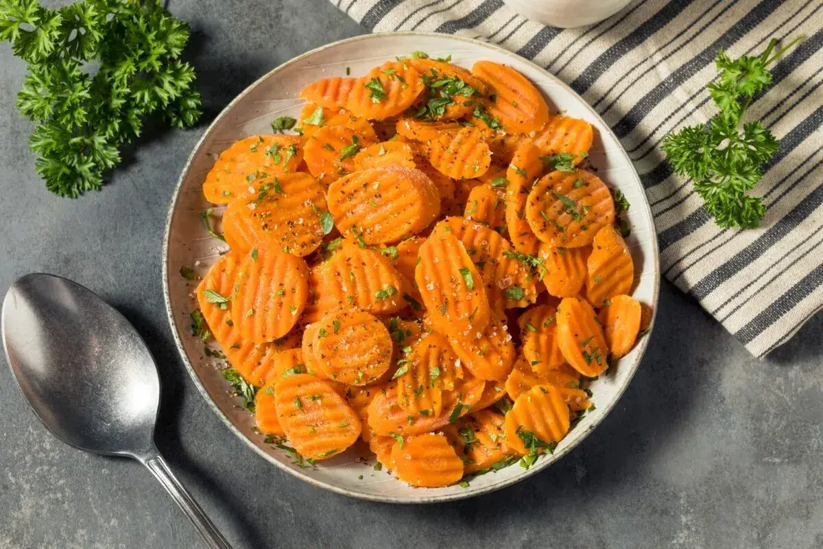 Carottes Vichy coupées en rondelles, saupoudrées d'herbes et de poivre, servies dans un plat avec une cuillère.