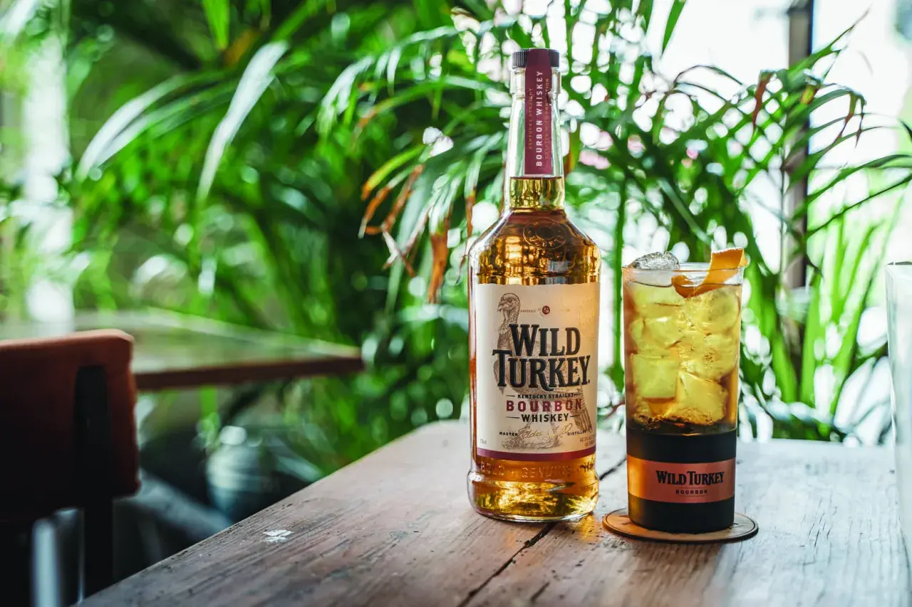 Un bicchiere di cocktail con bourbon Wild Turkey, ghiaccio e scorza d'arancia, accanto alla bottiglia.