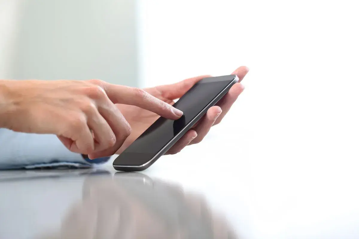 Dłonie trzymające smartfon, palec wskazujący dotyka ekranu. Szybko dowiesz się, jak doładować komuś konto ze swojego telefonu.