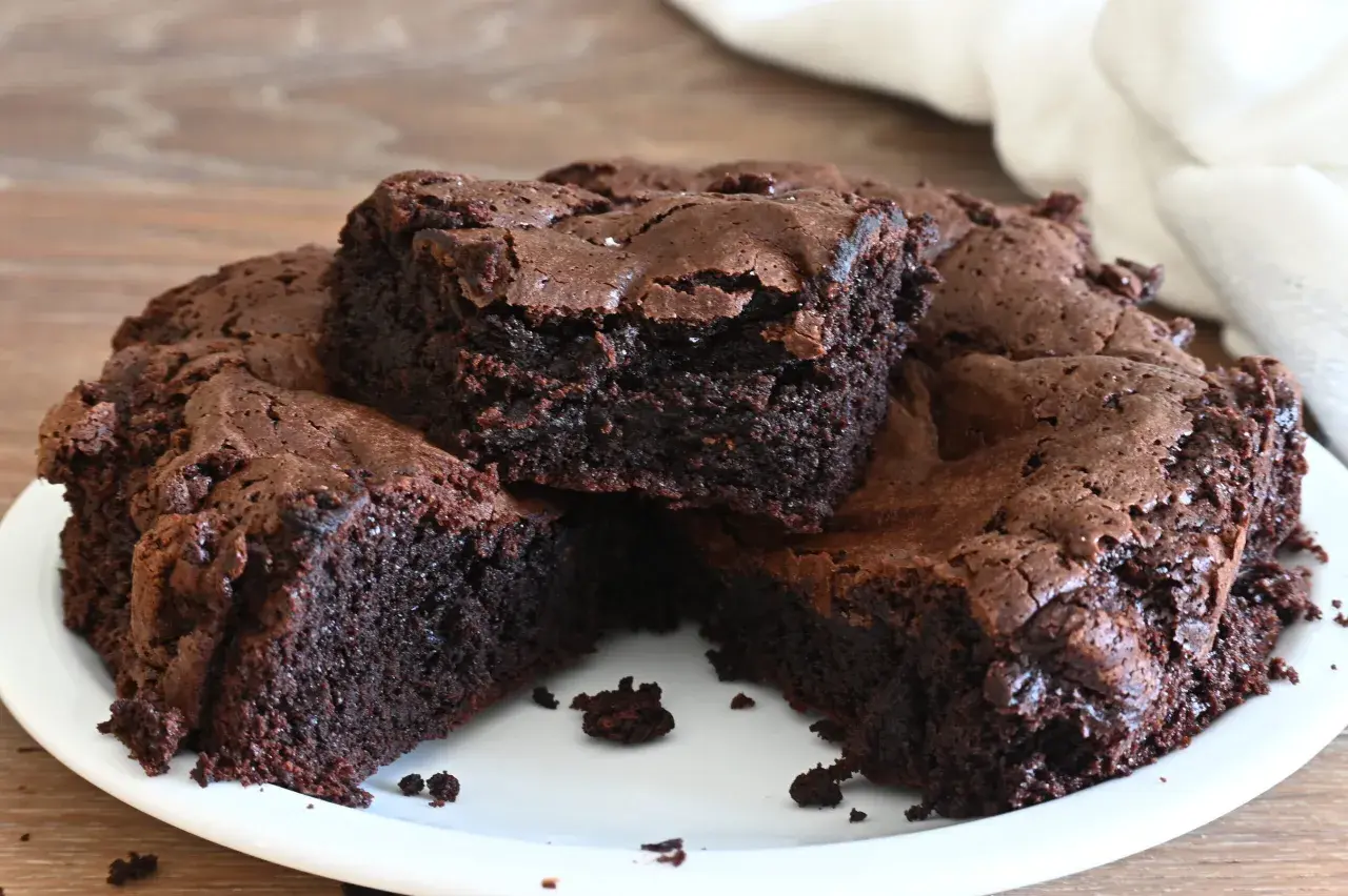Una torta cioccolatino ricca e umida, tagliata a fette su un piatto bianco. La superficie è leggermente screpolata, con cristalli di sale visibili.