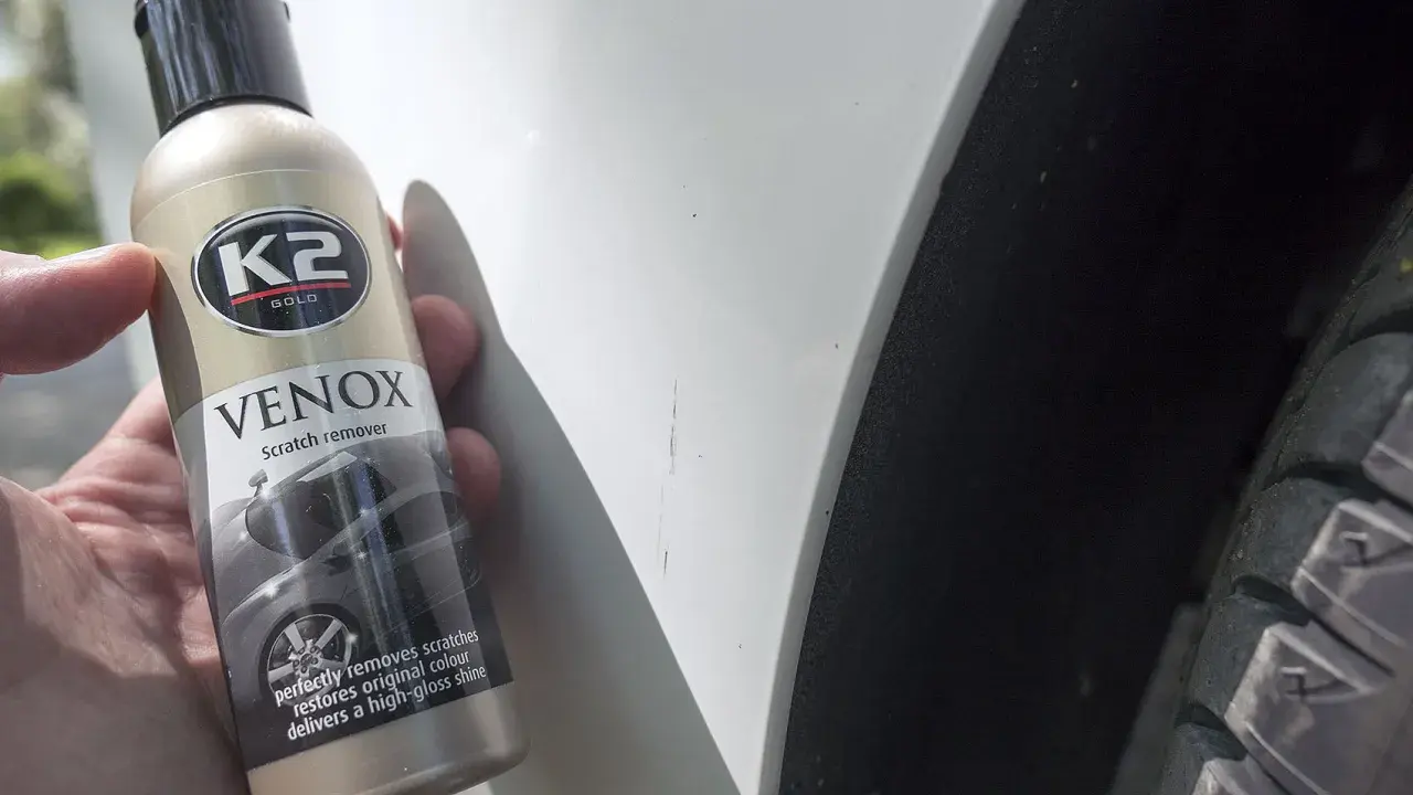 Jak usunąć rysy z samochodu domowym sposobem? Butelka K2 VENOX Scratch remover obok zarysowanego lakieru.