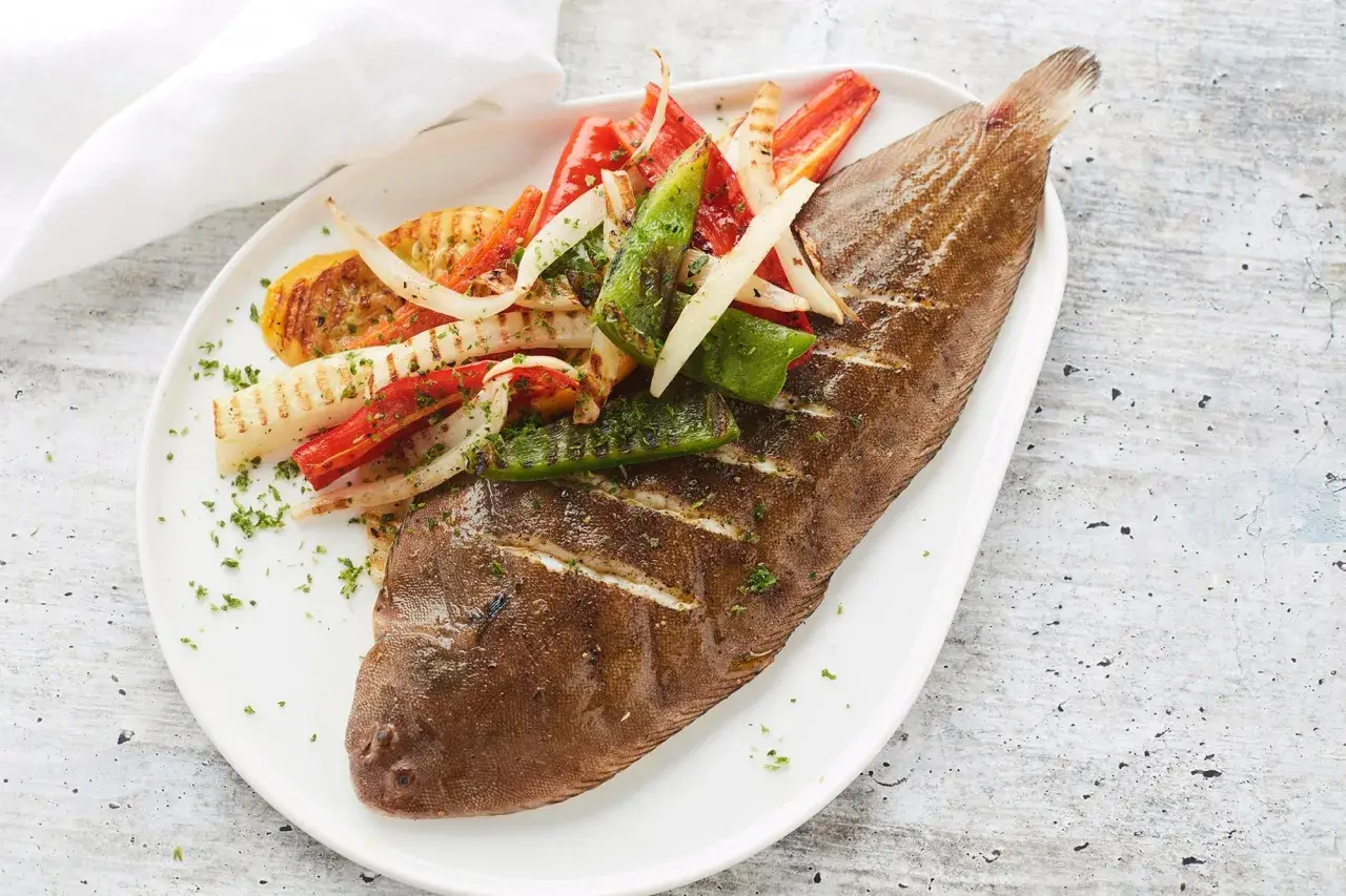 Sole grillé, garni de poivrons et d'oignons grillés, saupoudré de persil frais. Un plat savoureux et coloré.