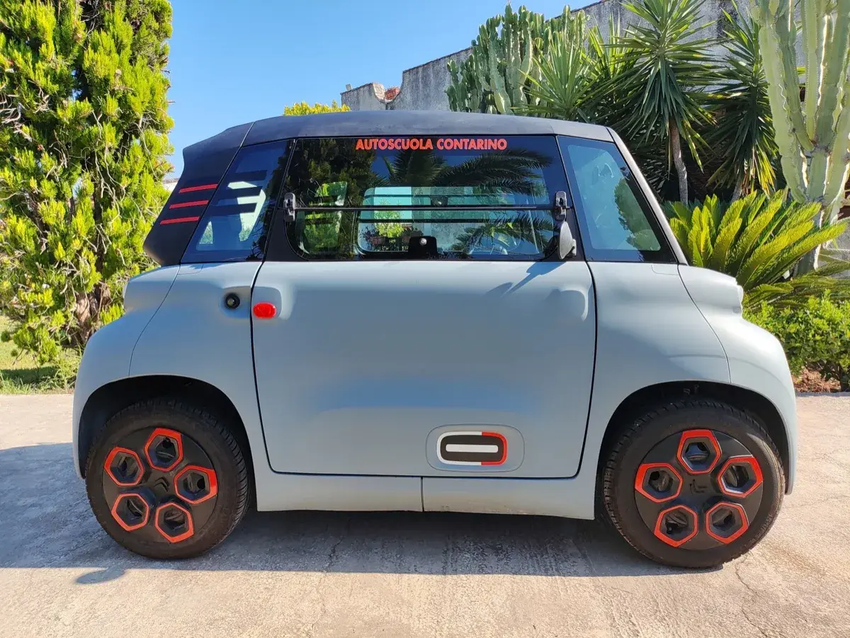 Citroën Ami grigia parcheggiata all'aperto, con dettagli rossi e neri. La scritta "Autoscuola Contarino" sul finestrino suggerisce un uso per l'apprendimento, con un'ottima **citroen ami autonomia** per la città.