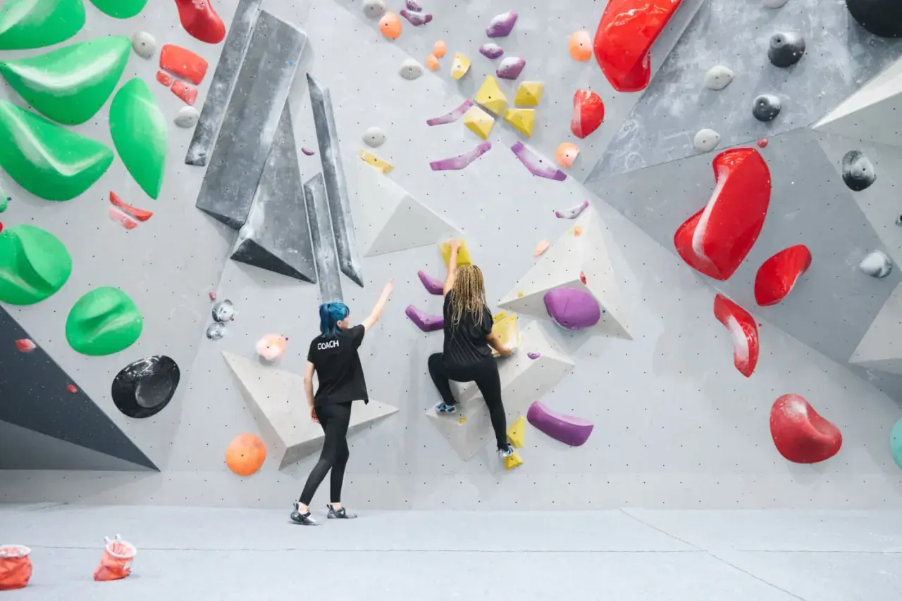 Zwei Frauen bouldern an einer Kletterwand. Eine gibt Anweisungen, die andere klettert. Das ist, was ist bouldern: eine Herausforderung für Körper und Geist.
