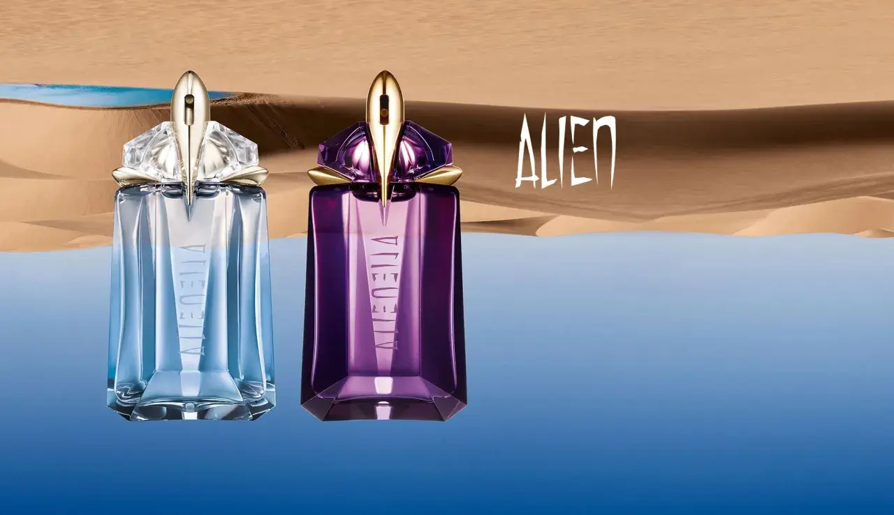 Dwa flakony Mugler Alien EDT: jeden błękitny, drugi fioletowy, na tle pustynnego krajobrazu z wodą.