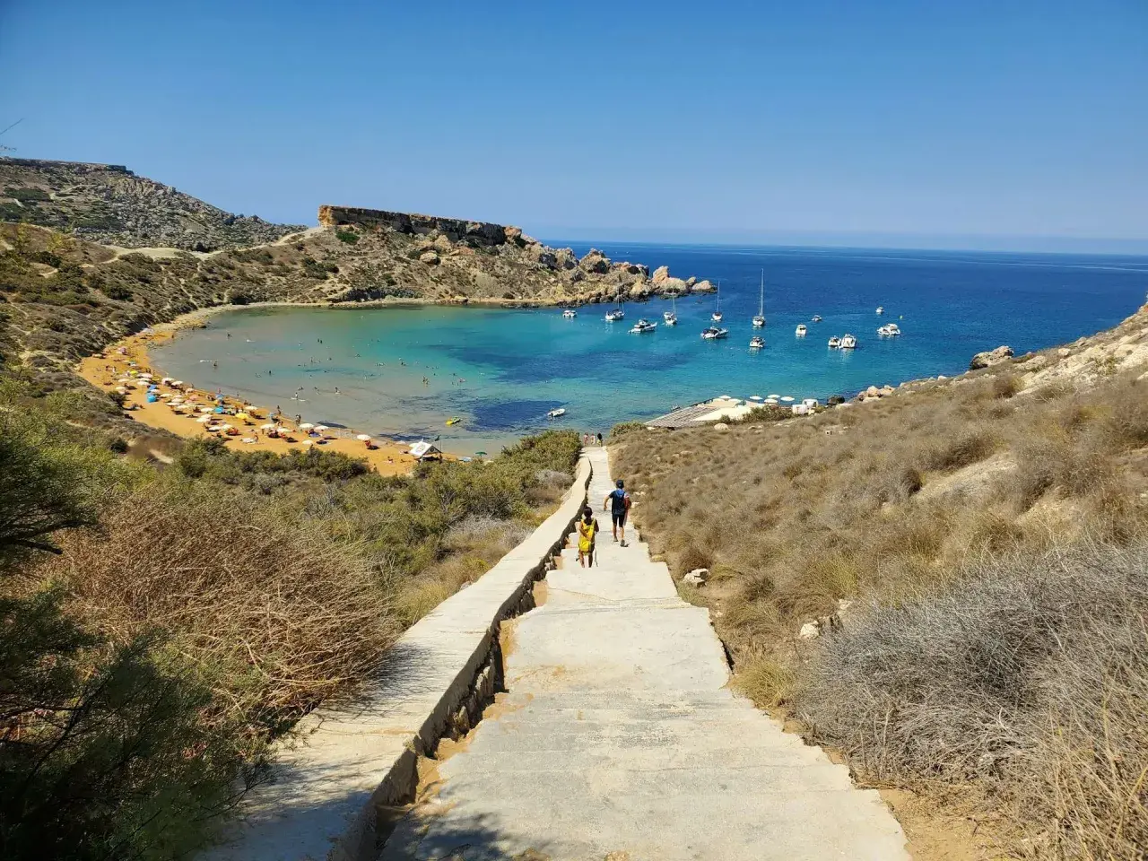 Malta, kwiecień: słoneczna pogoda zachęca do spaceru schodami w dół do zatoki z turkusową wodą i łodziami.