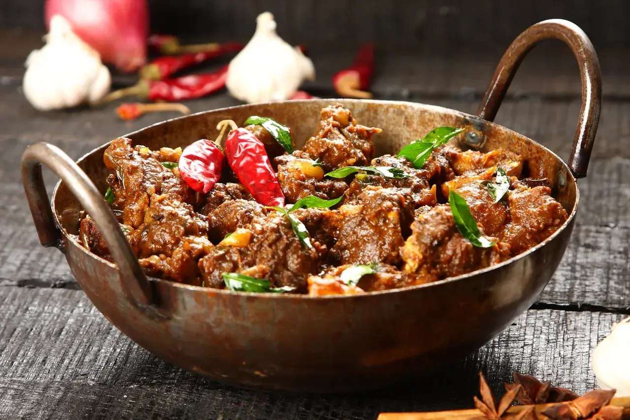 Aromatyczny gulasz z jagnięciny w miedzianym naczyniu, ozdobiony papryczkami chili i liśćmi curry.