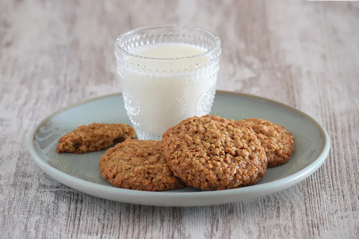 Un vaso de leche acompaña a unas deliciosas galletas de avena sobre un plato.