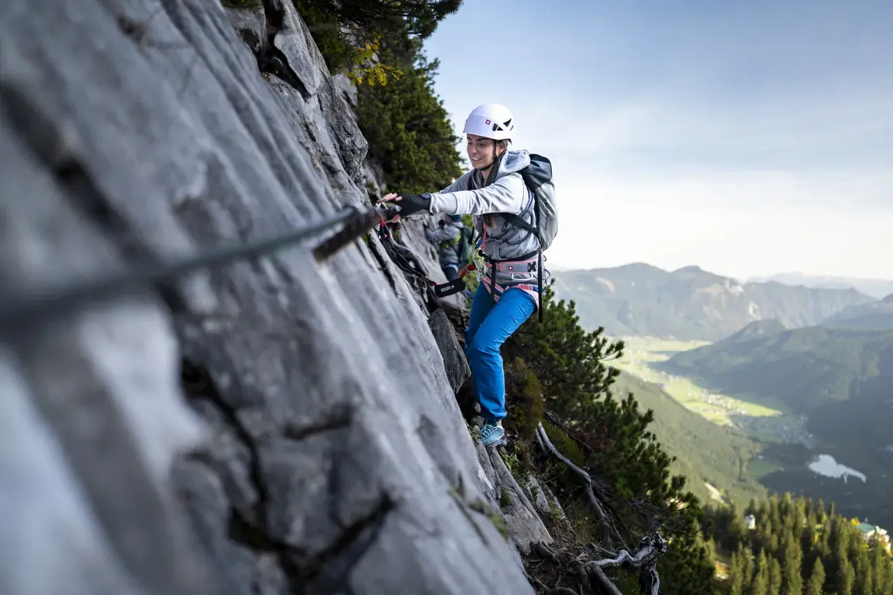 Uśmiechnięta kobieta na via ferrata dla początkujących, z widokiem na dolinę.