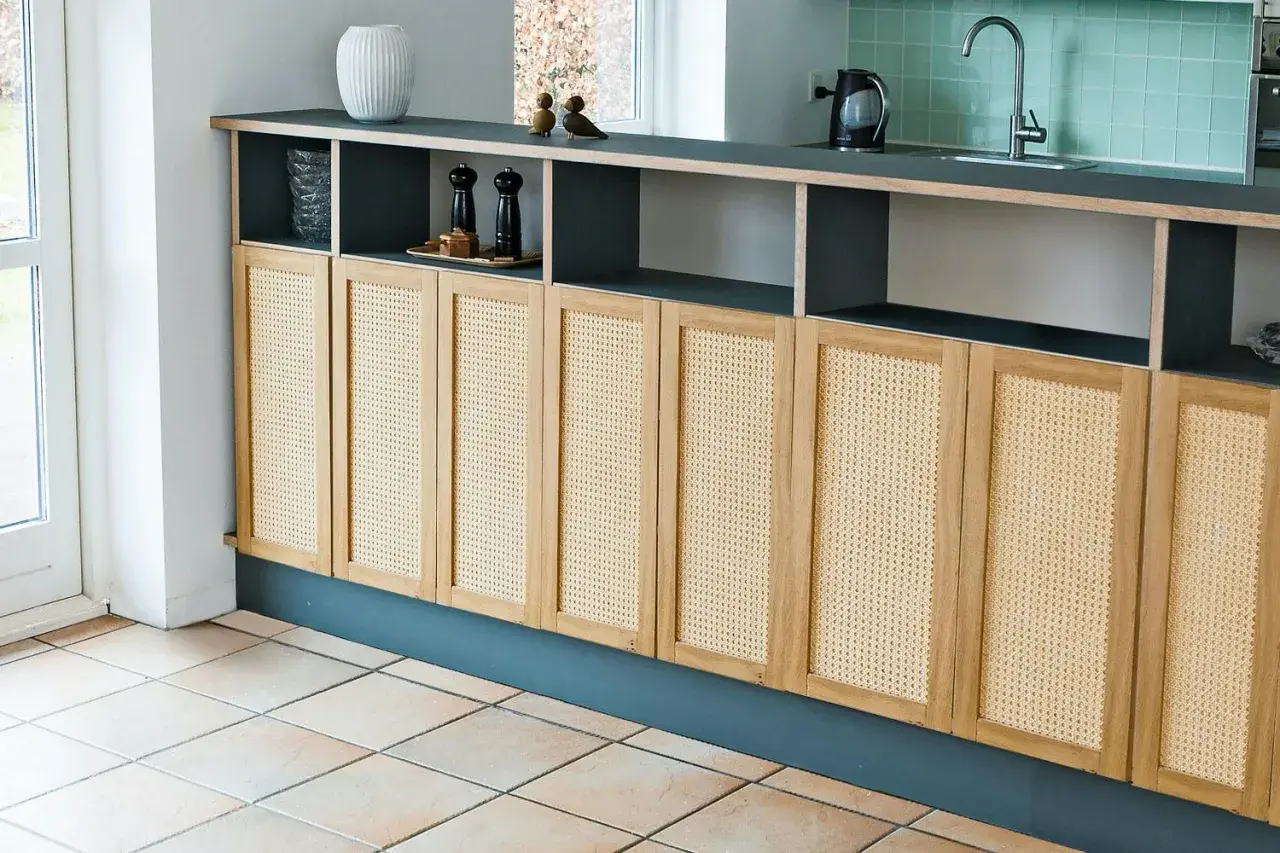Ett modernt kök med en lång bänk där man kan bygga skåp med rottingfronter. Över bänken finns öppna hyllplan med köksdetaljer.