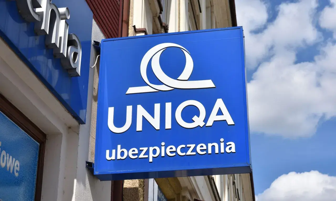 Niebieski szyld z logo i napisem "UNIQA ubezpieczenia". Firma UNIQA oferuje ubezpieczenia.