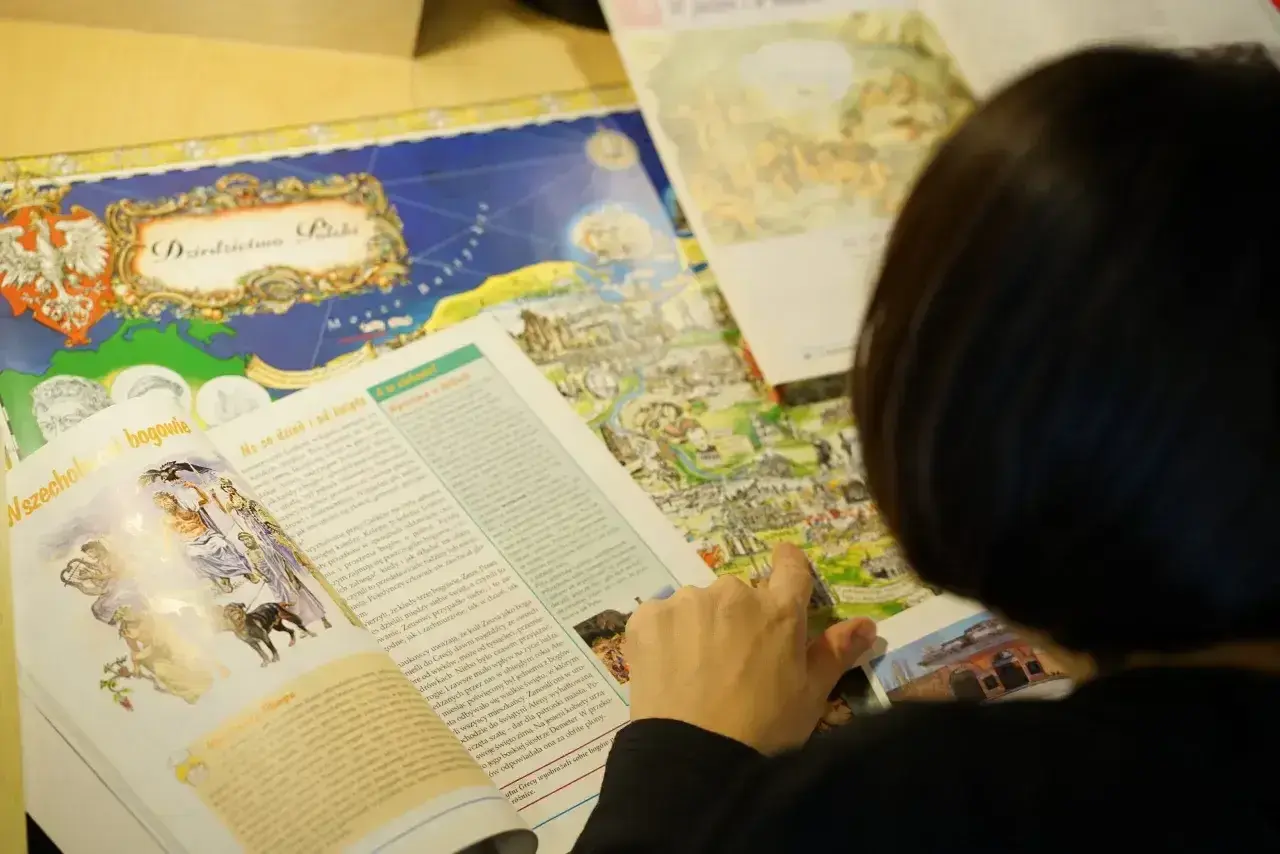 Osoba przegląda książkę z mapą Polski i ilustracjami mitologicznymi.