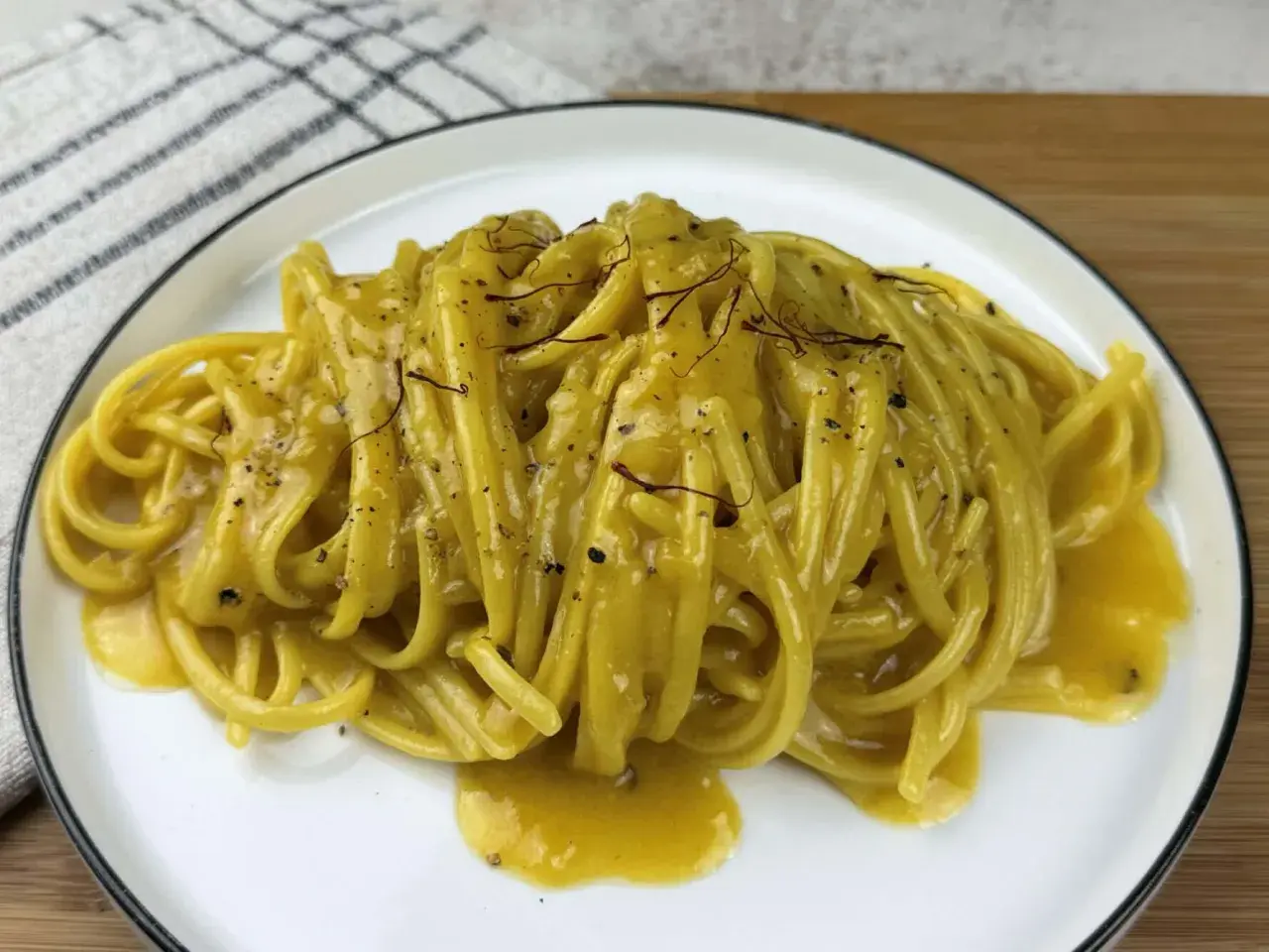Un piatto di pasta alla milanese cremosa, con fili di zafferano e pepe nero.