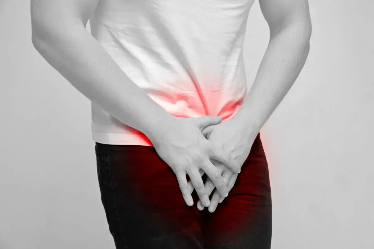 Mężczyzna trzyma ręce na podbrzuszu, gdzie widoczne są czerwone plamy bólu. Może to symbolizować dyskomfort związany z masowaniem prostaty.
