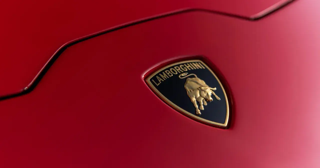 Złote logo Lamborghini z bykiem na czerwonym tle samochodu.