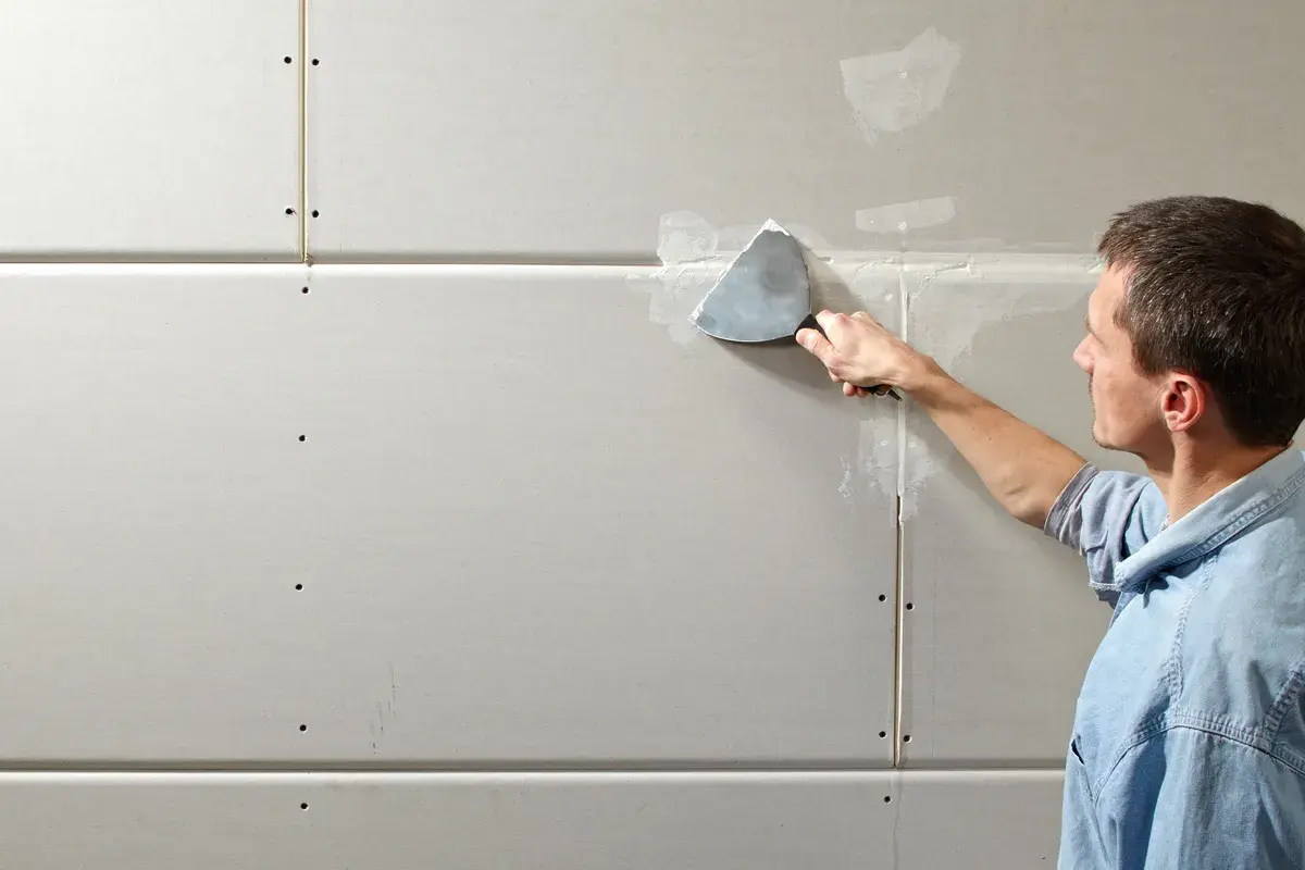 Mann spachtelt Rigipsplatten, um eine glatte Wand zu schaffen.