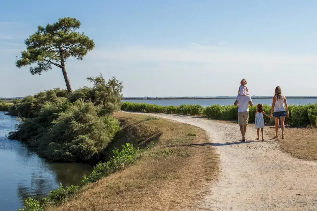 Une famille profite d'une randonnée à Arcachon, longeant un cours d'eau sous un ciel bleu.