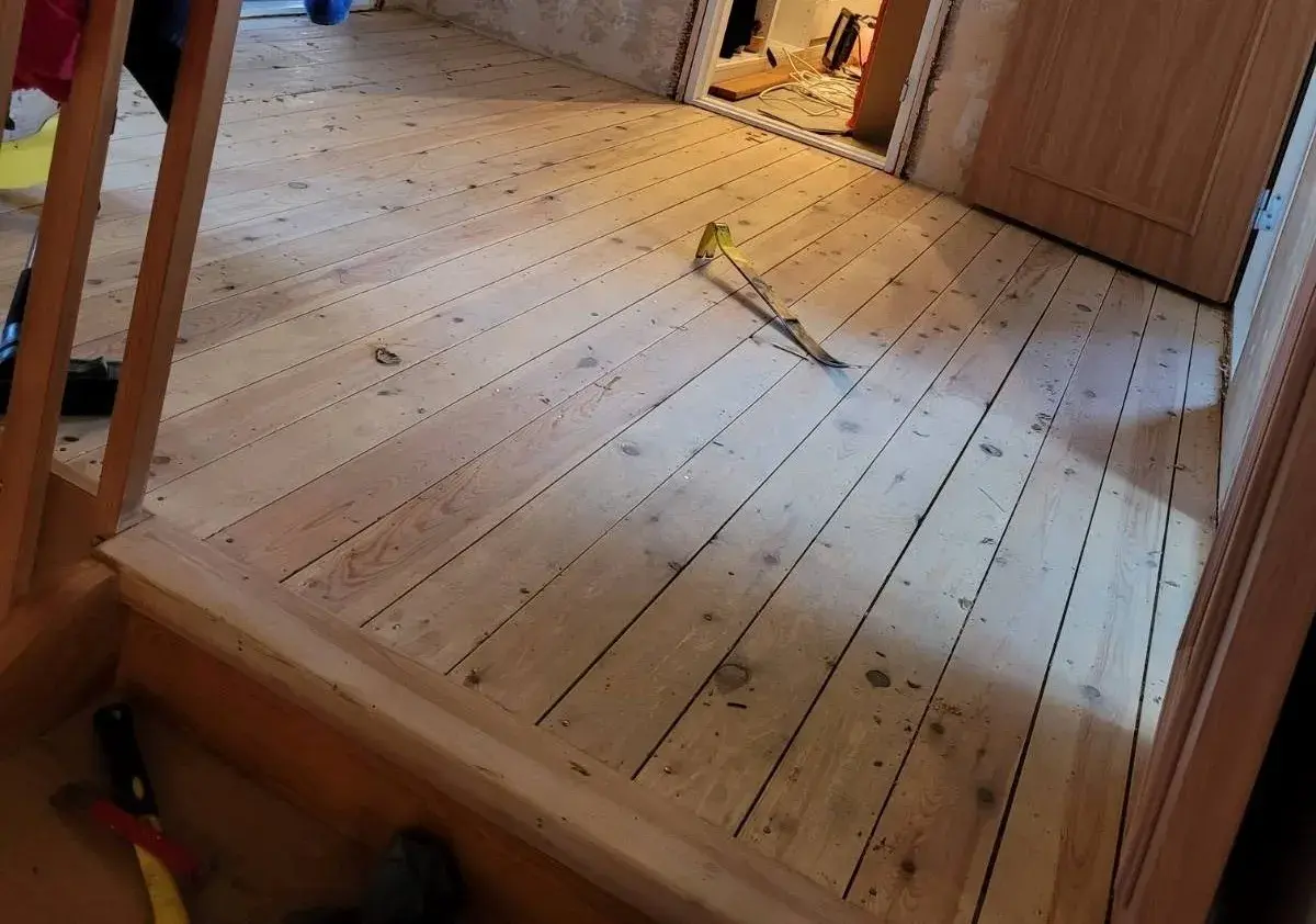 Ett rum med nylagt råspont golv. Ett verktyg ligger på golvet, redo för nästa steg i renoveringen.