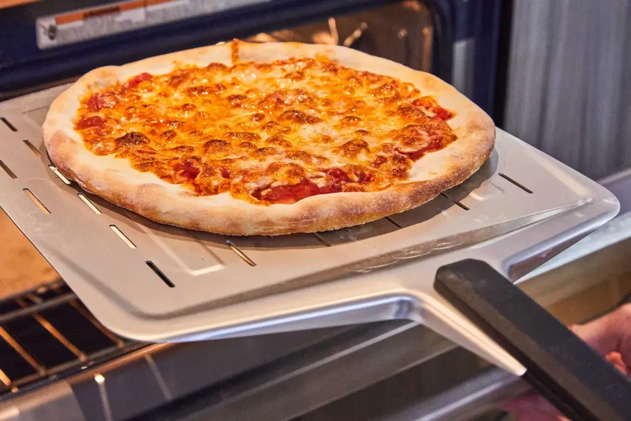 Une délicieuse pizza maison dorée et gratinée sort du four sur une pelle à pizza.