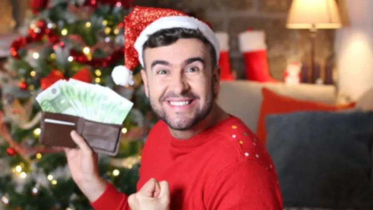Hombre con gorro de Papá Noel muestra billetera llena de dinero, como si soñara que le toca la lotería en Navidad.