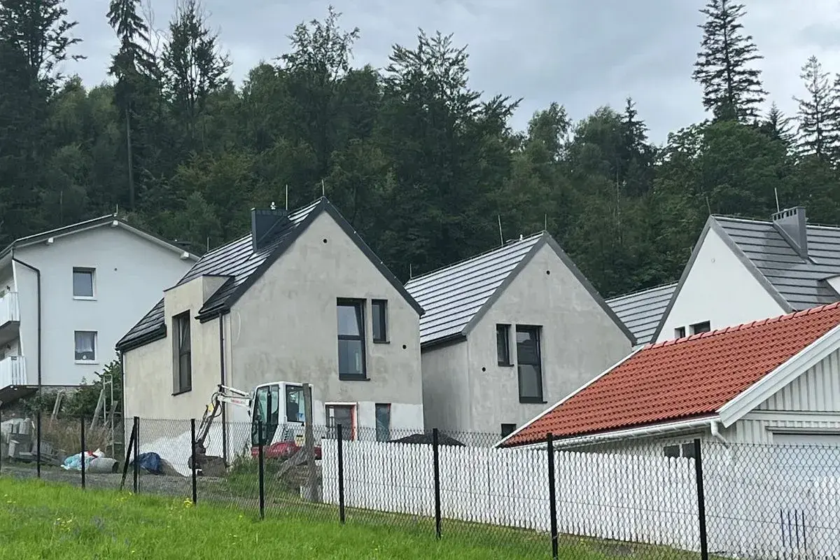 Nowe domy w stylu skandic hus, w budowie, z koparką na placu. W tle las.