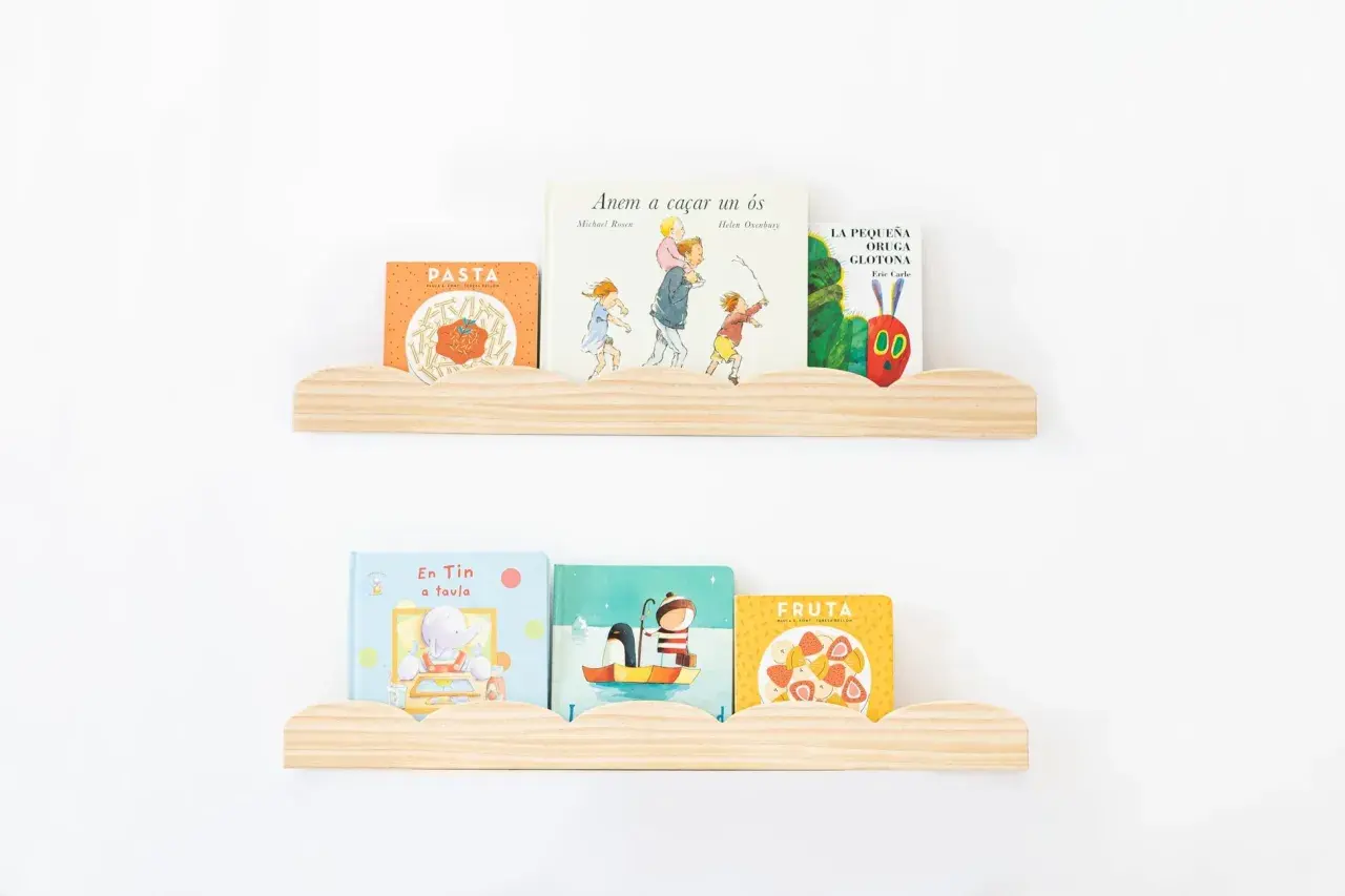 Dos estantes nube de madera con libros infantiles. En el superior: "Pasta", "Anem a caçar un ós" y "La pequeña oruga glotona". En el inferior: "En Tin a taula", un libro de pingüinos y "Fruta".