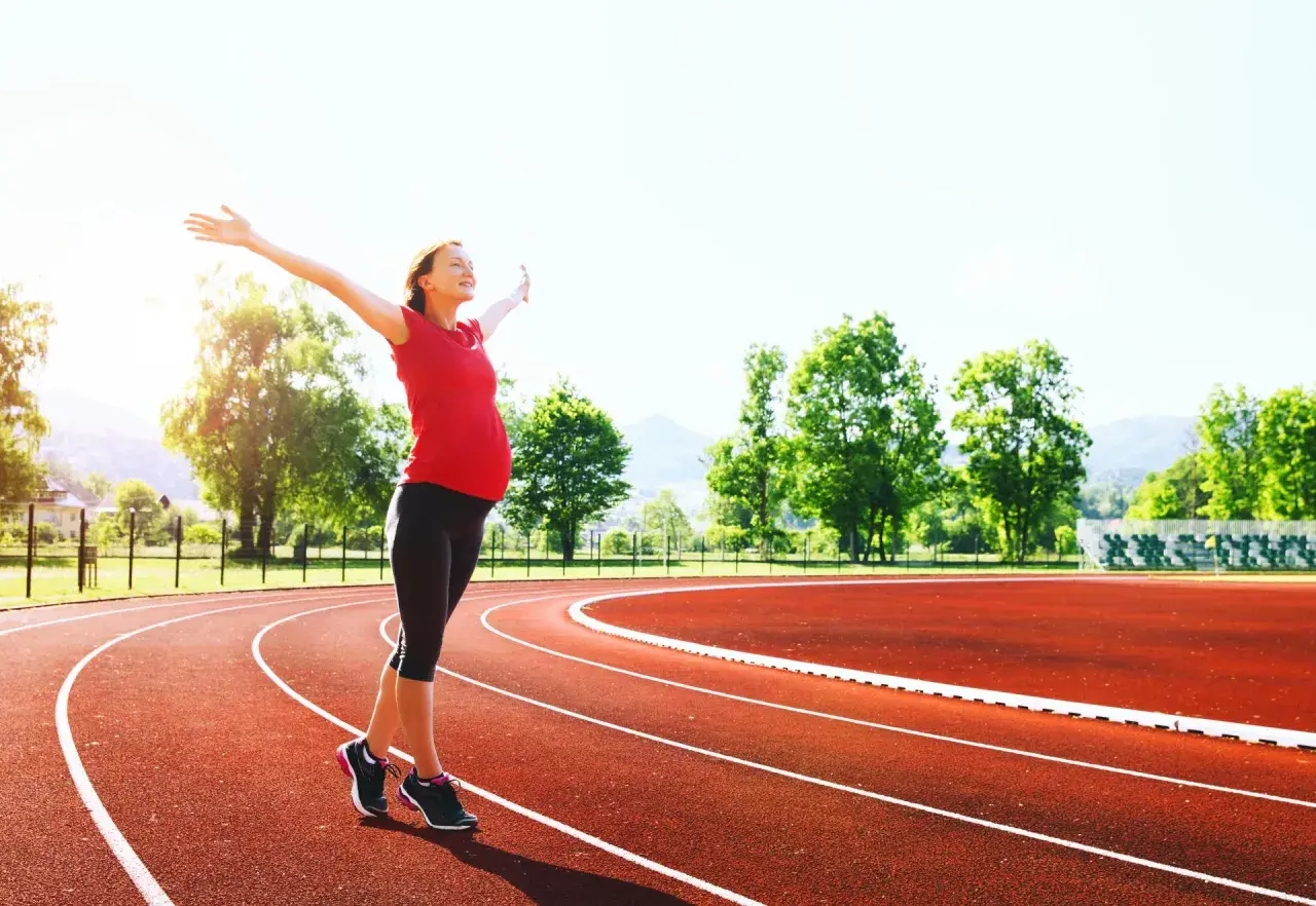 Donna incinta con le braccia aperte su una pista da corsa, dimostra che si può correre in gravidanza.