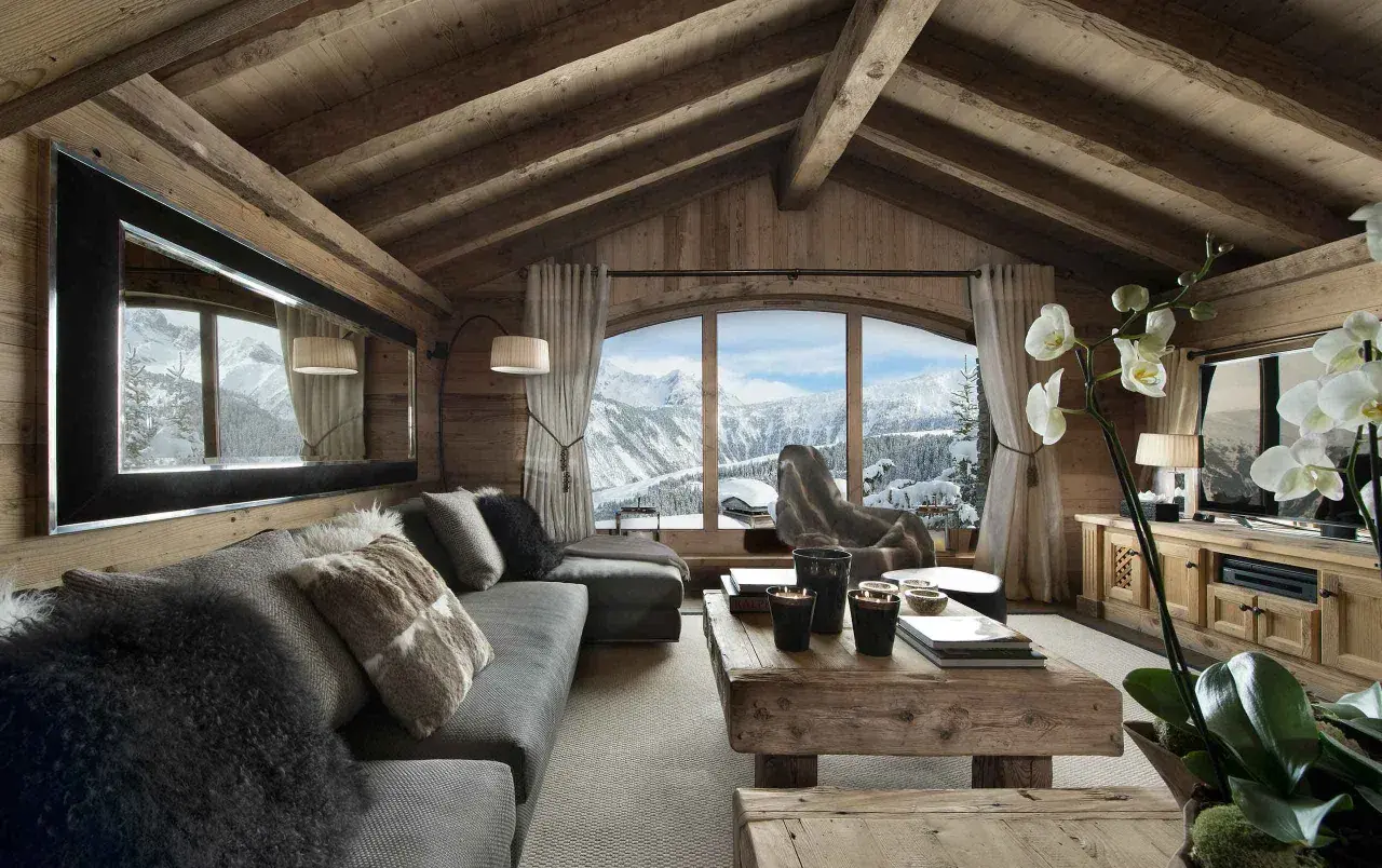 Gemütliches Wohnzimmer mit rustikaler Holzwand und Decke, einem großen Fenster mit Bergblick, einem Sofa mit Fellkissen und einem Holztisch. Luxus Chalet Inneneinrichtung.