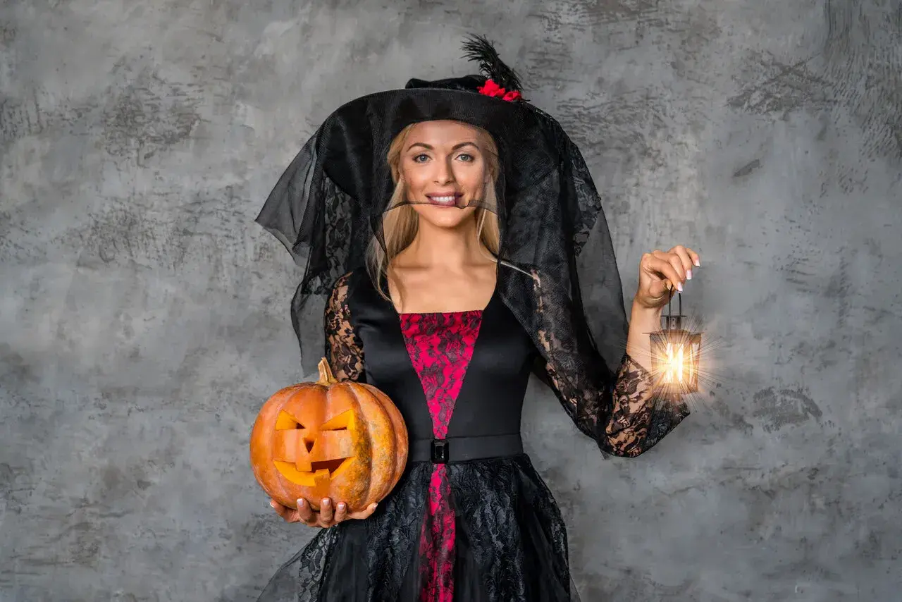 Kobieta w stroju czarownicy z dynią i latarenką. Inspiracja, jak się ubrać na Halloween.