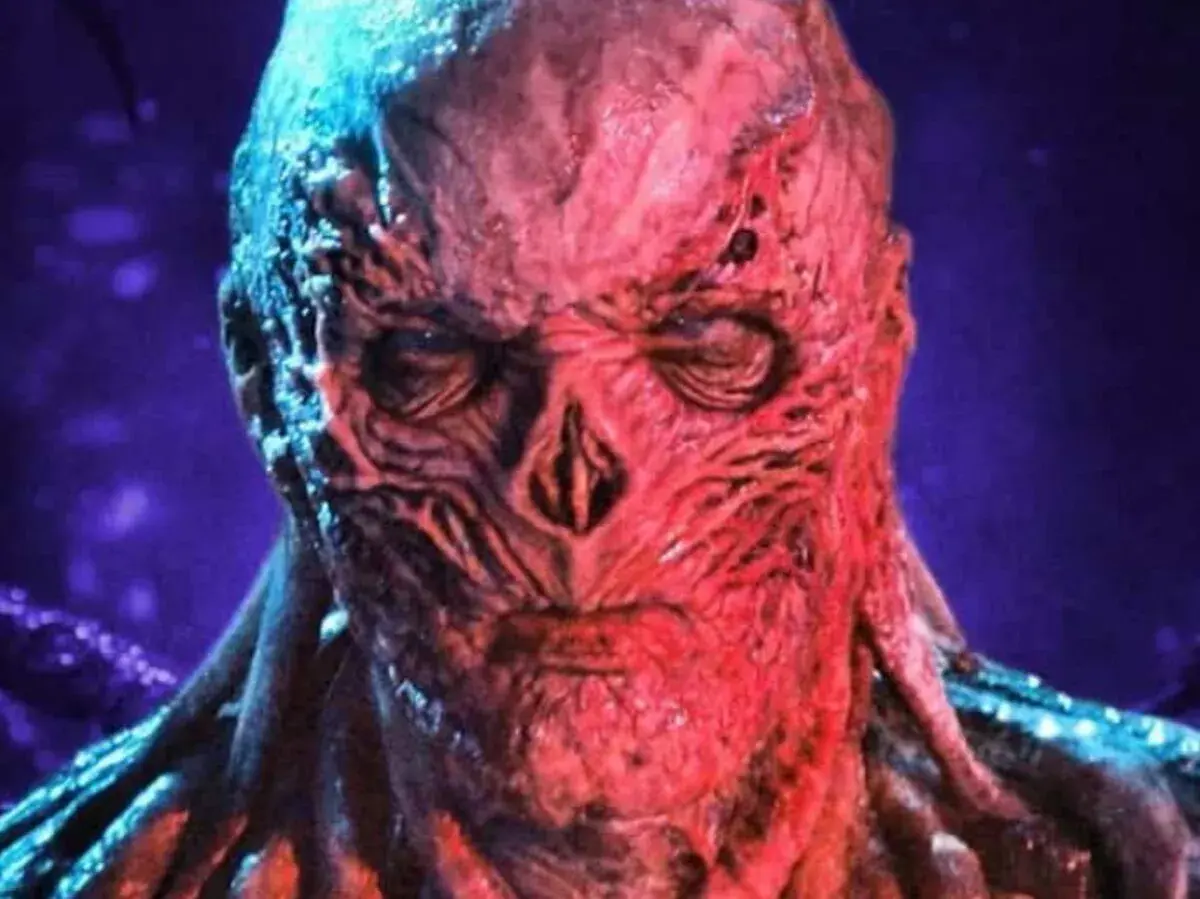Le visage déformé et rougeaud de Vecna, le monstre de Stranger Things, se détache sur un fond violet.