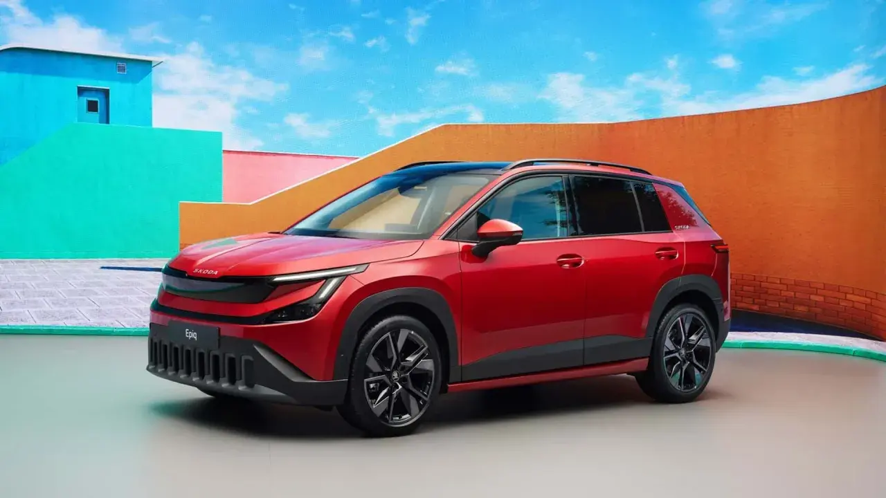 La Skoda Epiq rossa, un SUV compatto, si presenta con un design audace e moderno, circondata da un'architettura colorata e un cielo azzurro.