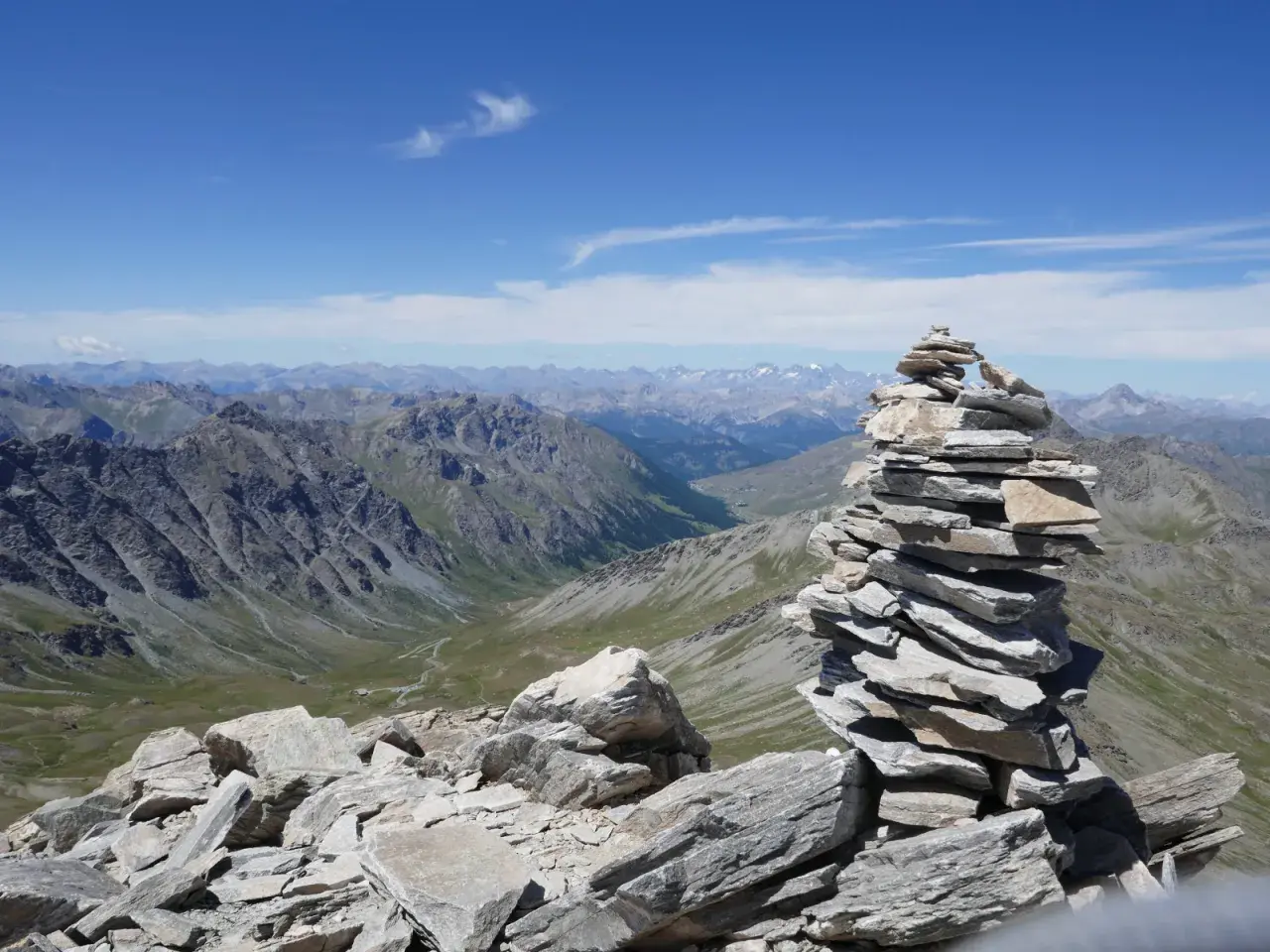 Un cairn, tel un tour du pain de sucre, domine un paysage de montagnes majestueuses sous un ciel bleu.