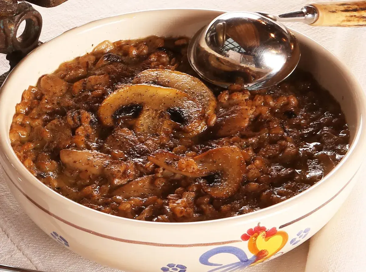 Una ciotola decorata con una ricca zuppa di farro e funghi, pronta per essere servita con un mestolo.