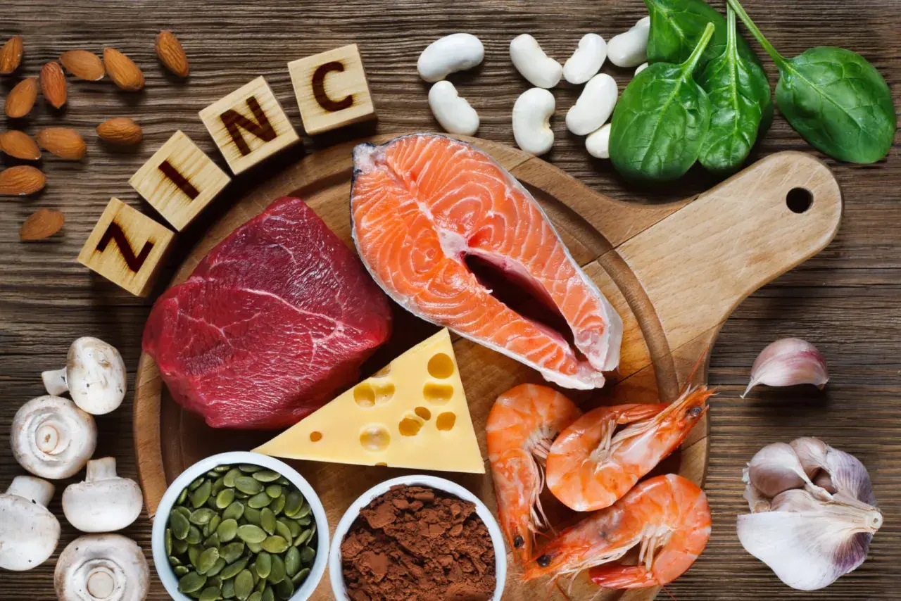 Zink-reiche Lebensmittel wie Rindfleisch, Lachs, Garnelen, Kürbiskerne, Käse, Spinat, Mandeln, Pilze und Knoblauch sind auf einem Holztisch arrangiert.