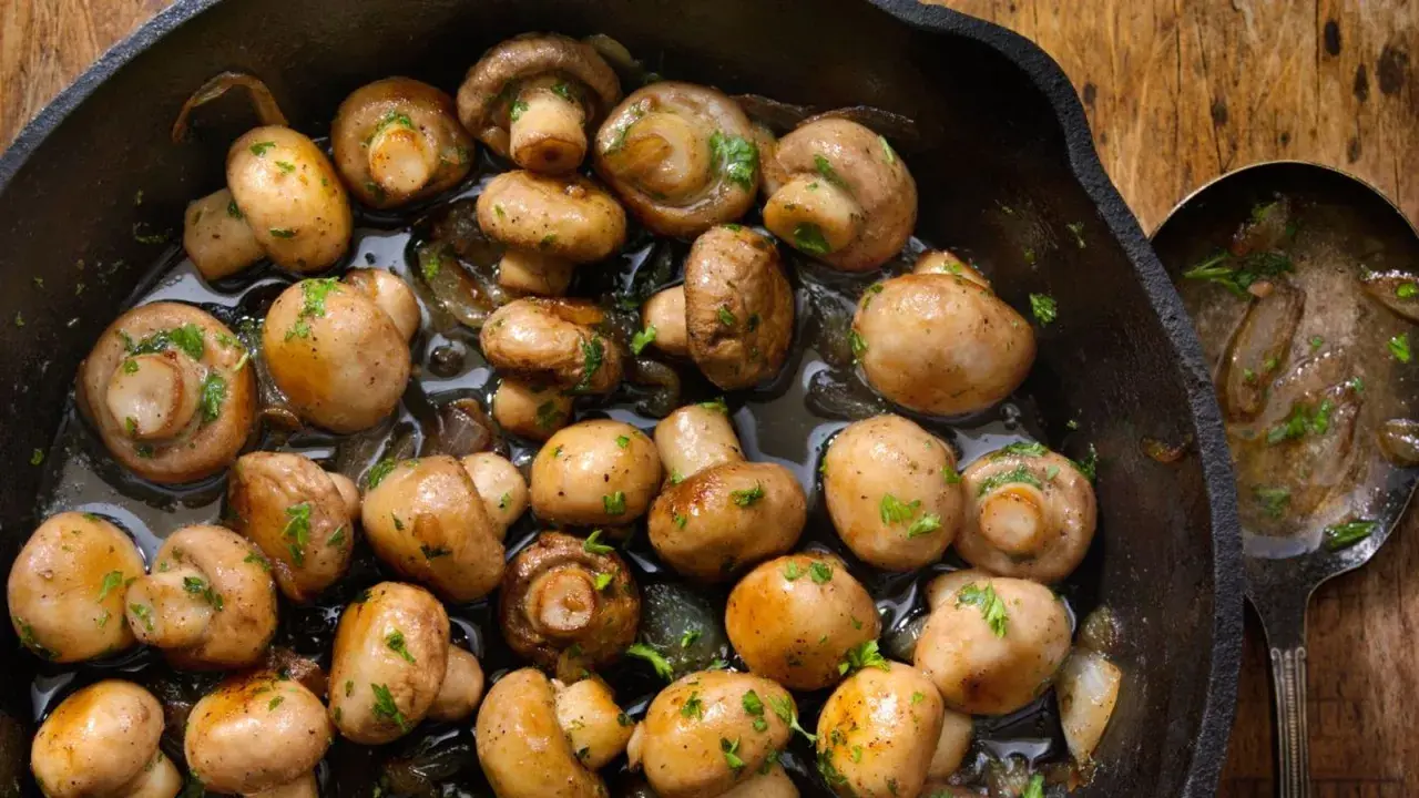 Champiñones al ajillo recién hechos en sartén de hierro fundido, con perejil picado y un toque de ajo.
