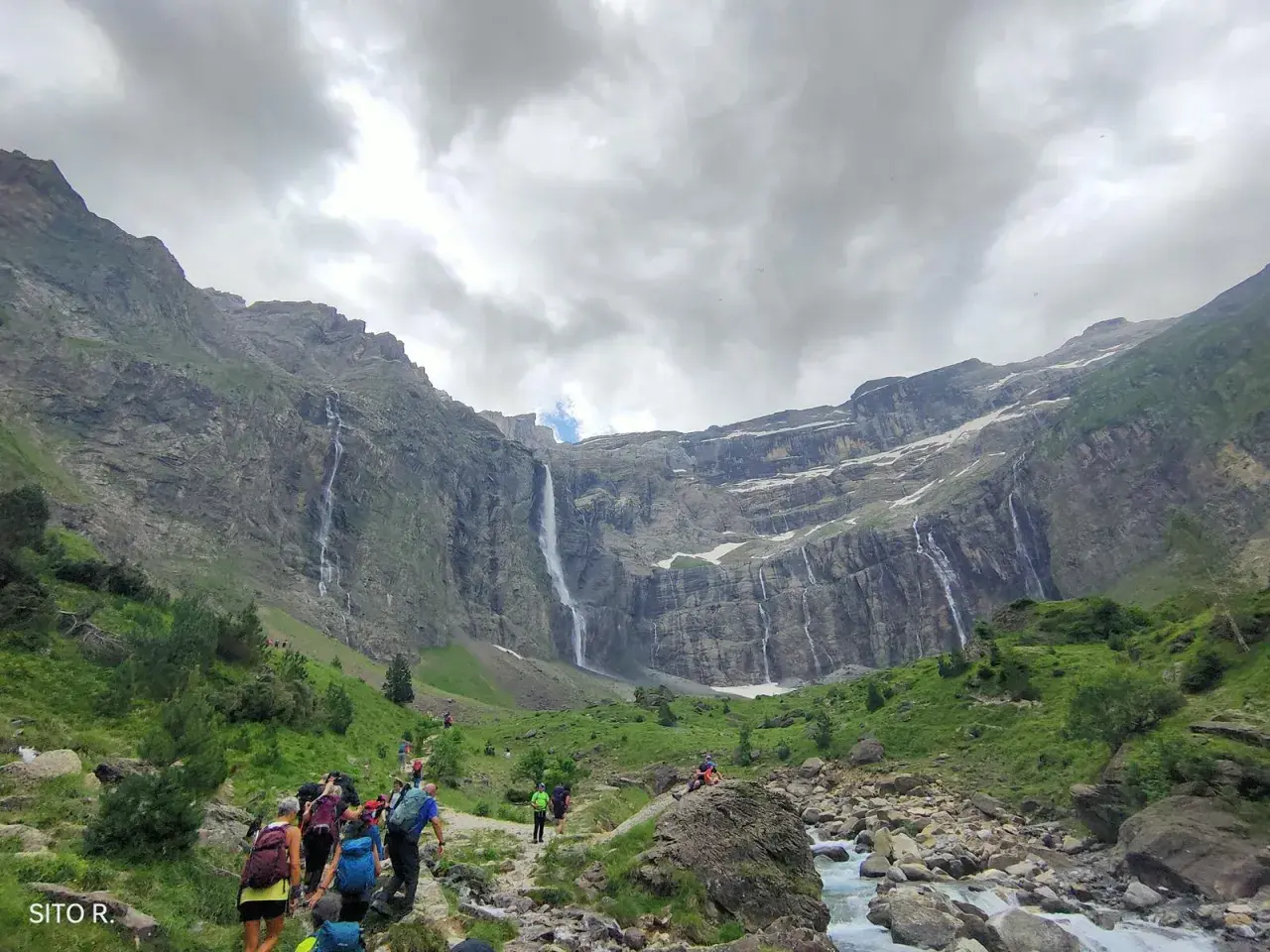 Senderos de Gavarnie: excursionistas caminan hacia impresionantes cascadas en un valle montañoso.
