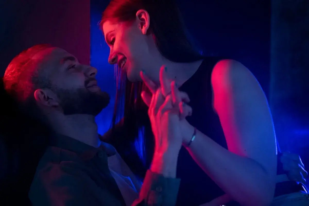 Para zbliża się do siebie w blasku neonów. Ich dłonie splatają się, tworząc intymną chwilę, która sugeruje seks bez penetracji.