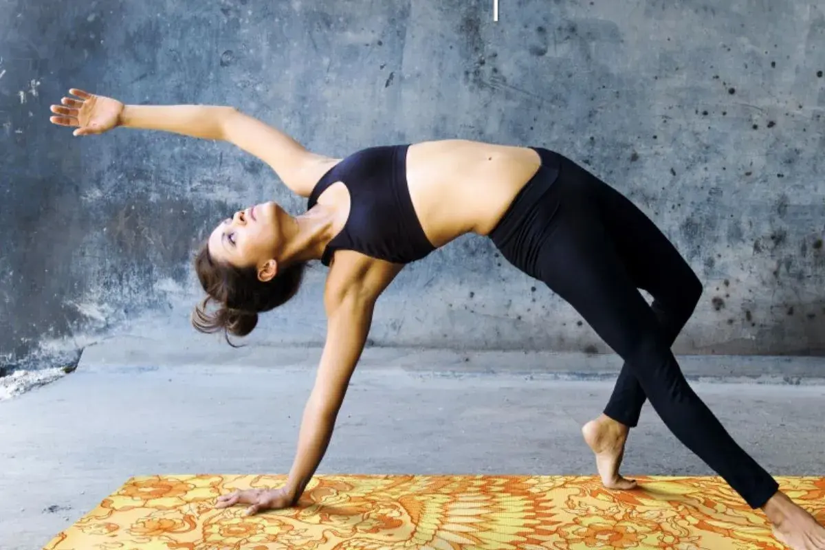 Donna in posizioni di yin yoga, con un braccio teso e il corpo arcuato all'indietro, su un tappetino colorato.