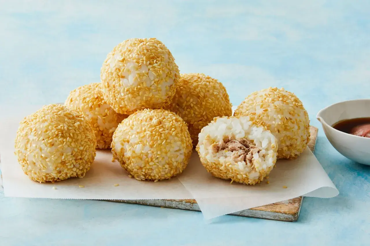 A delicious tuna bento box features rice balls coated in sesame seeds, with one cut open to reveal the tuna filling.