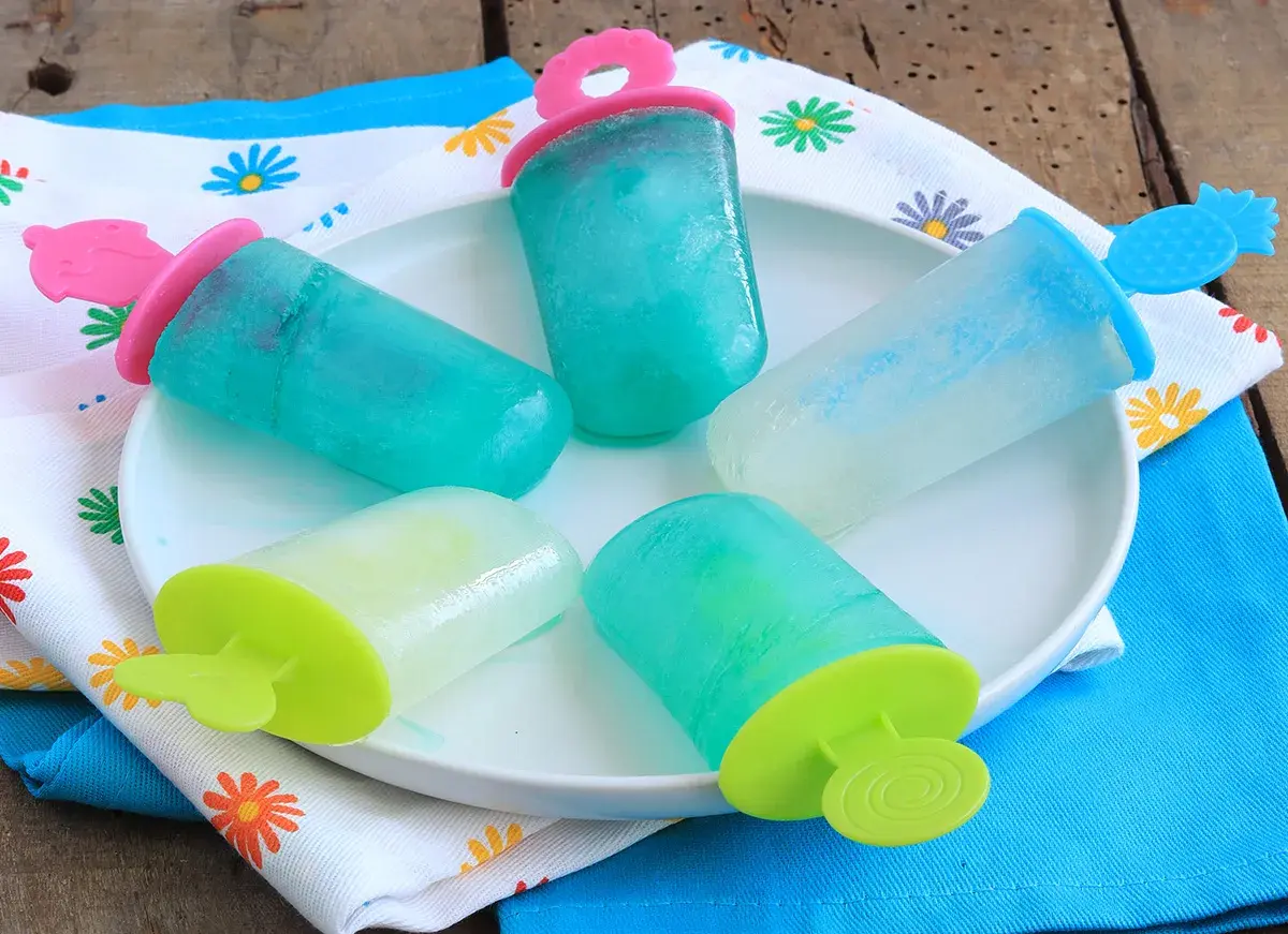 Cinque ghiaccioli senza zucchero, colorati e rinfrescanti, su un piatto bianco, pronti per un'estate sana e gustosa.