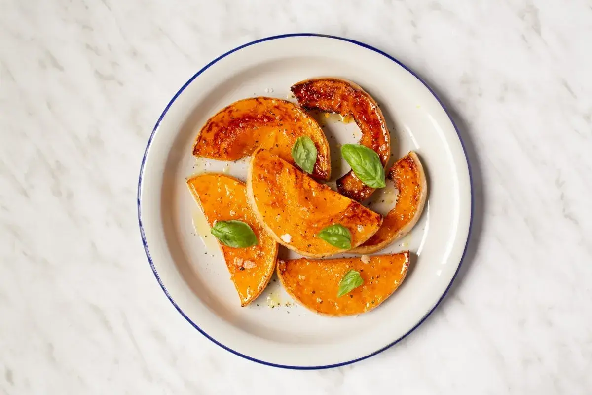 Rodajas de calabaza al horno, glaseadas y con hojas de albahaca fresca, servidas en un plato blanco con borde azul.