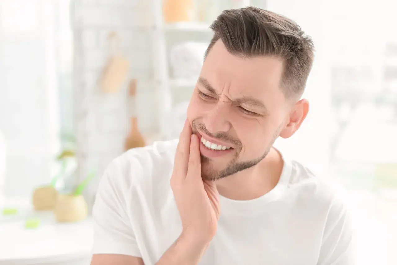 Uomo con mano sulla guancia, espressione di dolore ai denti, forse un problema al solco gengivale.